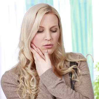 A young woman holding her cheek as she realizes she needs assistance from an emergency dentist in Lewisville