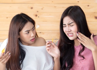 Two young woman eating chips and one looking as if she is in pain and pointing to her cheek