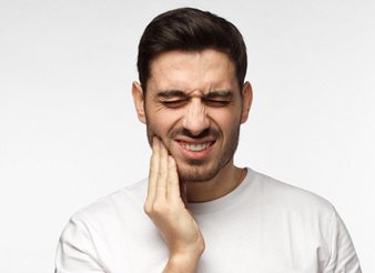 A young male holding his cheek and expressing immense pain