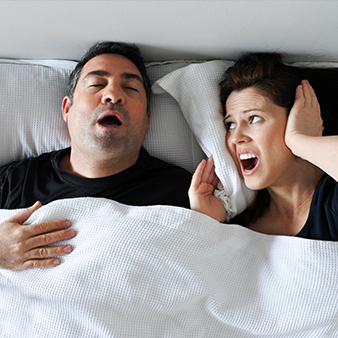 Woman covering ears next to snoring man in bed