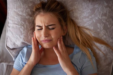 Woman rubbing her jaw while lying in bed.