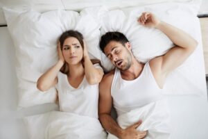 Woman covering her ears while her partner snores 