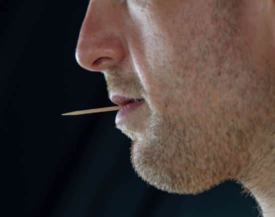 A man casually holding a toothpick in his mouth.