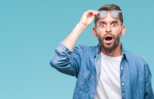 Man with a surprised expression raising sunglasses.