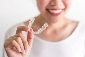 Nose-to-chest view of woman holding Invisalign with thumb and forefinger